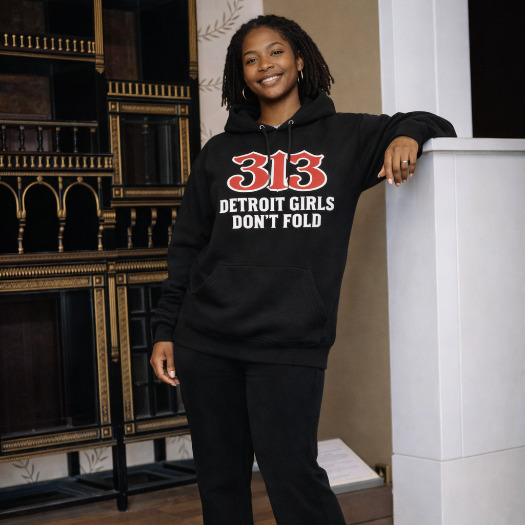 Person wearing a black hoodie with '313 Detroit Girls Don't Fold' text, standing indoors.