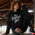 Person wearing a black hoodie with 'I'm a Detroit Girl' text, sitting on a concrete ledge.