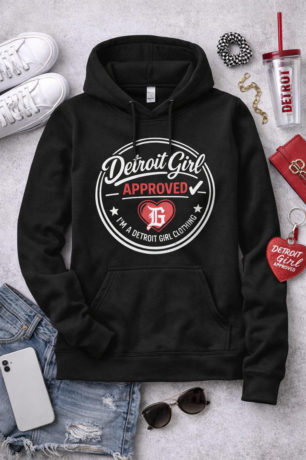 Black hoodie with 'Detroit Girl Approved' design on a gray surface with accessories.