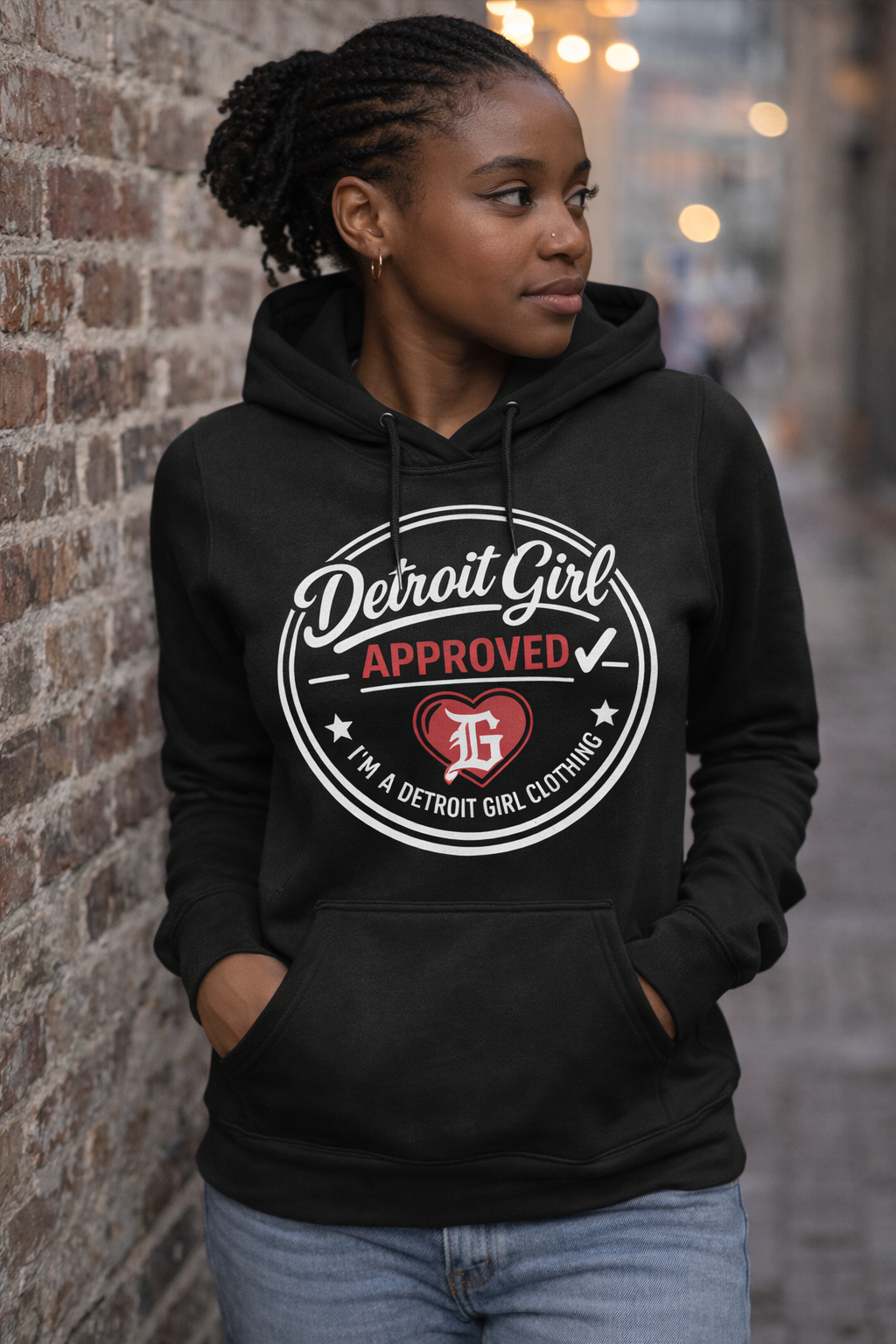 Person wearing a black hoodie with 'Detroit Girl Approved' design against a brick wall.