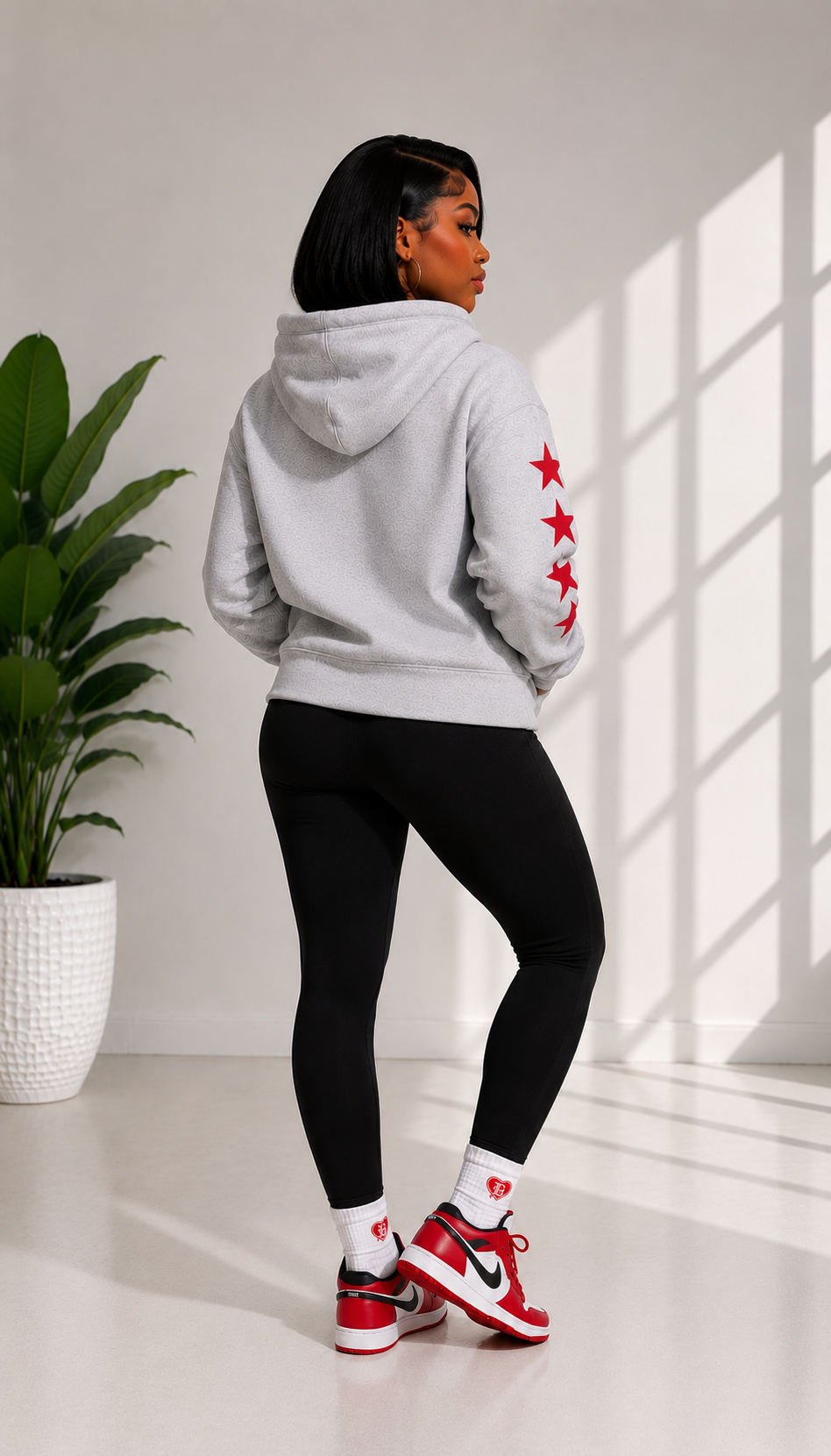 Person wearing a gray hoodie with red star designs, black leggings, and red sneakers in a bright room.