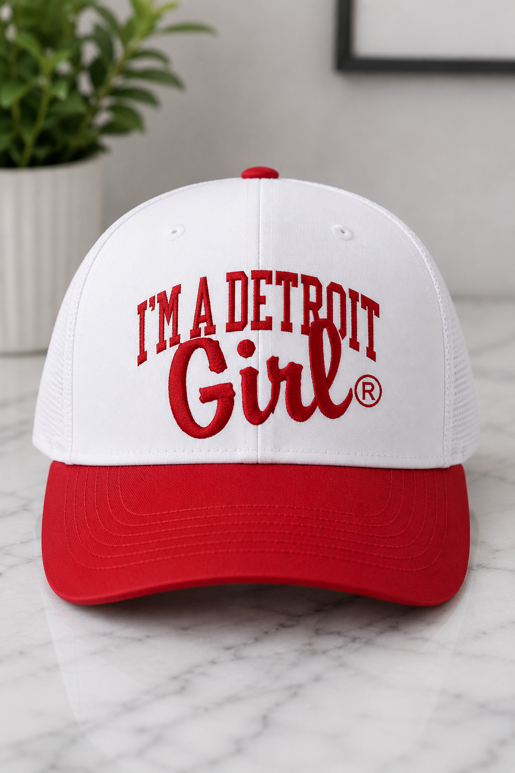 White cap with red brim and text 'I'm a Detroit Girl' on a marble surface.